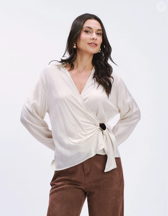A Camisa Cachecoeur Detalhe Fivela, da Zinzane, aposta na modelagem transpassada para valorizar a silhueta e reproduzir a elegância característica de Carolina Herrera