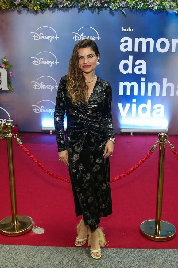 Vanessa Giácomo: apresenta-se com um vestido longo de veludo molhado escuro com estampa floral, decote em "V" transpardo e drapeado central, combinado com gargantilha brilhante e sandálias com detalhe em plumas amareladas