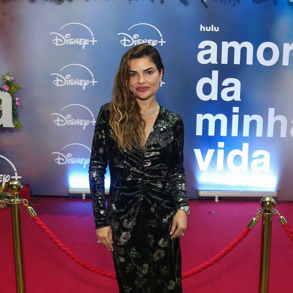 Vanessa Giácomo: apresenta-se com um vestido longo de veludo molhado escuro com estampa floral, decote em "V" transpardo e drapeado central, combinado com gargantilha brilhante e sandálias com detalhe em plumas amareladas
