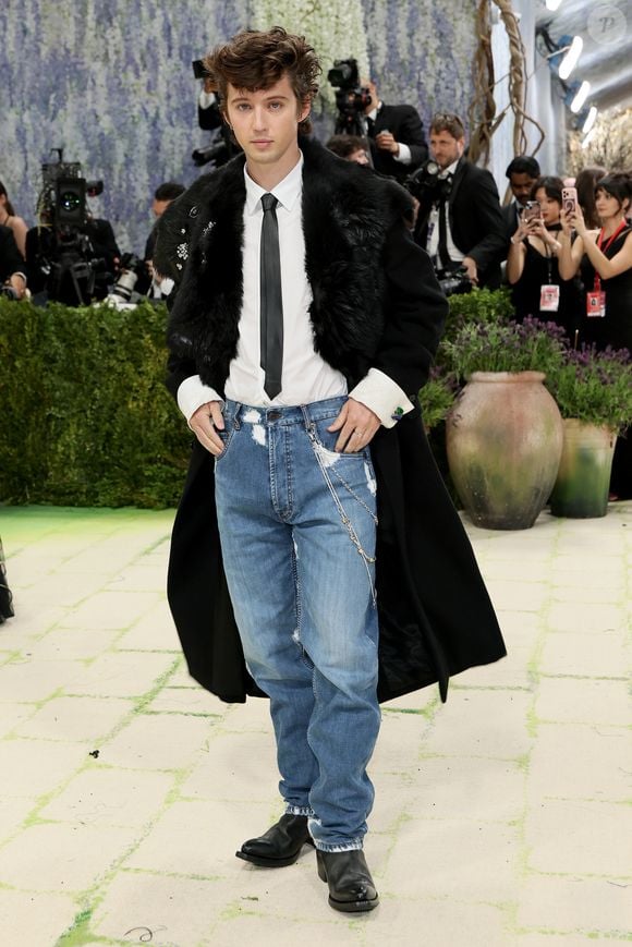 Look de passear no shopping? Troye Sivan no Met Gala 2026 apostou no streetwear, com jeans, camisa branca e gravata, sobrepostos por um casaco alongado