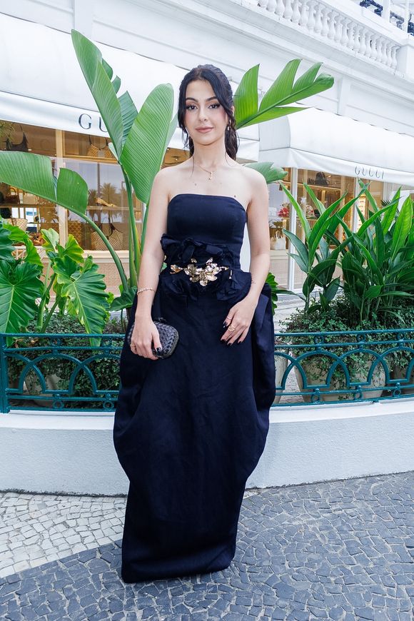Klara Castanho trouxe uma proposta de alta costura com um vestido preto escultural de tafetá. A peça, sem alças, destaca-se pelo volume orgânico e arquitetônico nos quadris, criando uma silhueta 'ampulheta' moderna e imponente. O detalhe mestre da produção é o cinto largo com aplicações de flores tridimensionais e um ornamento central metálico em dourado, que quebra a monocromia com um toque artístico