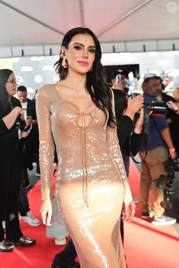 Gabi escolheu um vestido midi dourado com paetês, mangas longas e um decote profundo com amarração frontal. O tecido brilhante refletia a luz lindamente, realçando sua presença no red carpet. O cabelo solto em ondas e os brincos grandes completaram o look com um toque glamouroso e moderno.