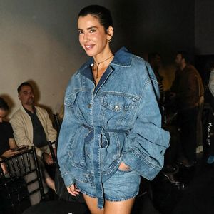 Camila Coutinho traz uma proposta total denim moderna, composta por uma jaqueta jeans oversized de lavagem azul-média com mangas volumosas e amarração na cintura pelo próprio tecido, sobreposta a um mini short jeans correspondente. Para criar contraste, o look foi finalizado com scarpins brancos de salto alto e tira no tornozelo