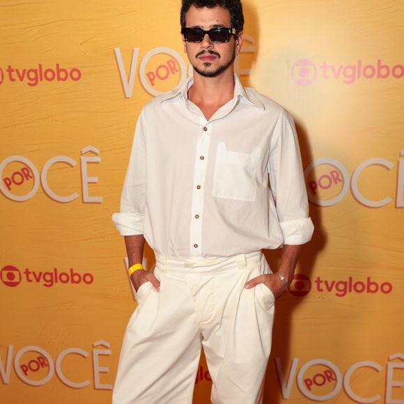 Rodrigo Lelis investe na elegância monocromática off-white/branca com camisa social levemente aberta no peito e com mangas dobradas nos antebraços, combinada a uma calça de alfaiataria de cintura alta com pregas e modelagem ampla. Óculos de sol pretos e sapatos sociais brilhantes completam o visual