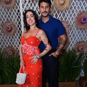 Lucas Pizane e Giovanna Lima: Giovanna elegeu um vestido longo vermelho com estampas florais brancas, recorte frontal cut-out e amarração no busto, combinado a uma bolsa de mão texturizada em pérolas. Lucas Pizane harmonizou com uma camisa polo azul-marinho lisa, calça preta de corte reto e sapatos mocassim bicolores em preto e branco