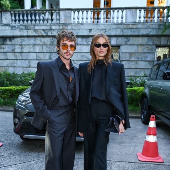 João Lucas acompanhou a estética em um terno cinza-chumbo de caimento largo, usado com a camisa entreaberta para um ar rebelde e descontraído. Seus óculos de lentes alaranjadas e os sapatos de bico quadrado reforçam a identidade de moda vanguardista que define a nova geração da elite criativa brasileira