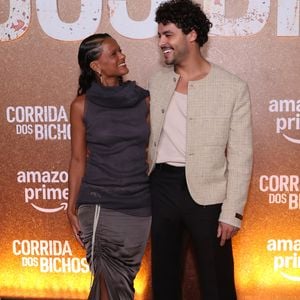 Em pose conjunta, Thainá Duarte e Matheus Abreu harmonizam produções de moda autoral e contemporânea. Enquanto a atriz exibe a silhueta ajustada e assimétrica em tons de cinza com cauda fluida, o ator complementa a composição com a textura encorpada do tweed claro sobre alfaiataria escura