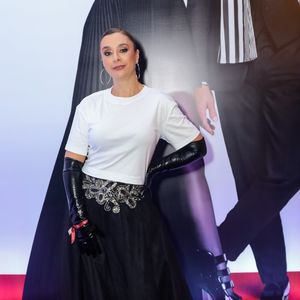 Cátia Fonseca utilizou uma proposta que mescla o básico com o dramático. O look traz uma t-shirt branca de algodão com corte reto, inserida sob uma saia longa de tule preto de várias camadas e cintura alta, decorada com um bordado prateado de motivos orgânicos na região do cós. O elemento de maior impacto são as luvas de ópera em vinil preto que cobrem quase todo o braço, trazendo um ar performático à produção