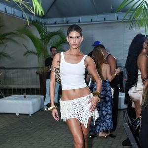 Laura Fernandes usou uma regata cropped branca básica de tecido canelado combinada com uma minisaia de crochê vazada off-white de cintura baixa e barra assimétrica. A produção praiana e casual contou com bolsa de ombro com estampa animal print (zebrada), braceletes artesanais largos nos dois braços e sandálias de salto fino com tiras de dedo brancas
