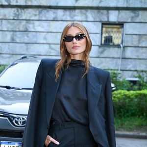 Sasha optou por um conjunto total black composto por um blazer oversized de ombros estruturados sobre uma blusa de gola alta em seda e calças de corte reto impecável, finalizando com óculos escuros estilo cat-eye e uma bolsa de mão estruturada