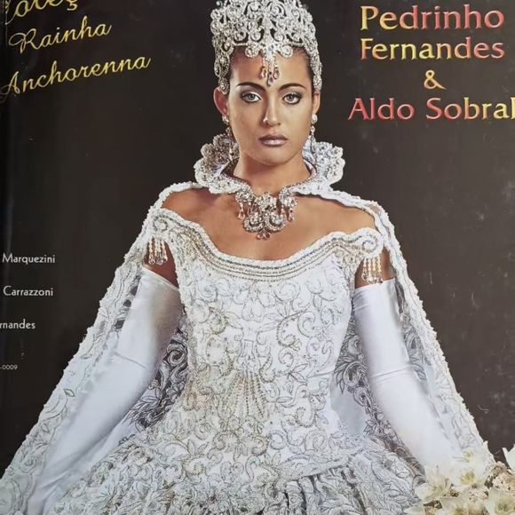 9.  Vestido com muito brilho

Esse é o ápice da noiva imperial: um vestido todo branco com bordados prateados e pedrarias cristalizadas que se espalham em padrões geométricos e florais pelo corpete e pela saia volumosa. A modelagem tem ombros levemente caídos, trazendo feminilidade e sofisticação.

As luvas longas brancas reforçam o ar aristocrático, enquanto a capa bordada adiciona movimento e realeza. O ponto máximo é a coroa dramática, toda em prata com aplicações em cascata que descem pela testa, um detalhe teatral e digno de editorial de passarela.
