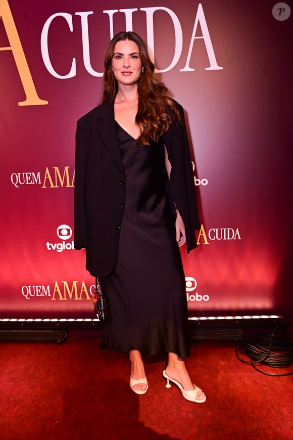 Lívia Inhudes: a atriz escolheu o minimalismo chic do slip dress de cetim preto, sobreposto por um blazer de alfaiataria estruturado jogado casualmente sobre os ombros. O visual, que une a delicadeza da seda com o corte masculino, foi finalizado com tamancos brancos de salto taça, criando um contraste visual limpo e elegante