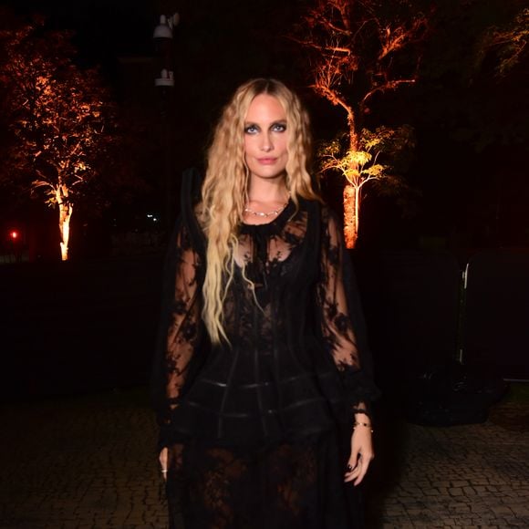 Schneider Moura usa vestido longo preto de renda com transparência. A peça apresenta mangas compridas bufantes e transparentes de renda, um corpete ajustado com detalhes de fitas horizontais na cintura e uma saia longa fluida também em renda transparente sobre uma base escura