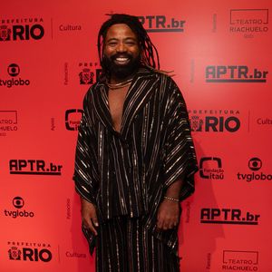 Exbanjando estilo, Douglas Silva vestiu um conjunto oversized texturizado em tom preto com listras verticais metalizadas em dourado. A túnica ampla de decote profundo foi combinada a uma calça pantalona de mesmo padrão, finalizada com um colar rígido dourado rente ao pescoço e sapatos tratorados robustos de verniz
