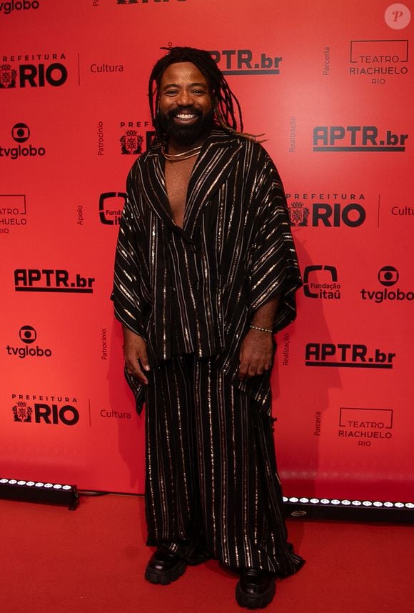 Exbanjando estilo, Douglas Silva vestiu um conjunto oversized texturizado em tom preto com listras verticais metalizadas em dourado. A túnica ampla de decote profundo foi combinada a uma calça pantalona de mesmo padrão, finalizada com um colar rígido dourado rente ao pescoço e sapatos tratorados robustos de verniz