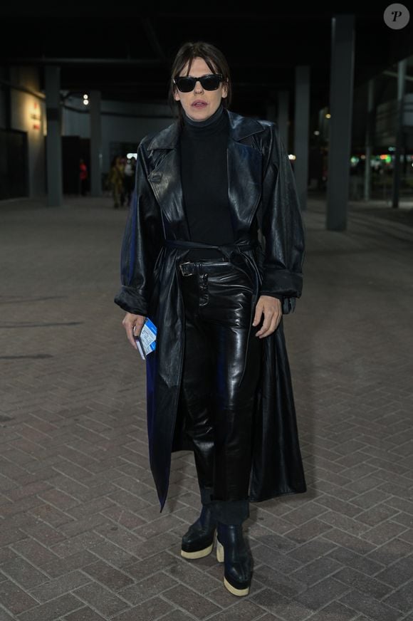 Bárbara Paz: look rocker monocromático em couro preto com sobretudo longo, blusa de gola alta, calça de couro brilhante, óculos escuros e botas de plataforma alta com sola clara