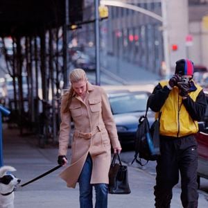 Na vida real, Carolyn Bessette, esposa de John F. Kennedy Jr., foi fotografada em 1998 enquanto passeava com seu cachorro usando o icônico casaco bege da Prada, peça que se tornaria um dos símbolos mais elegantes de seu estilo minimalista dos anos 90