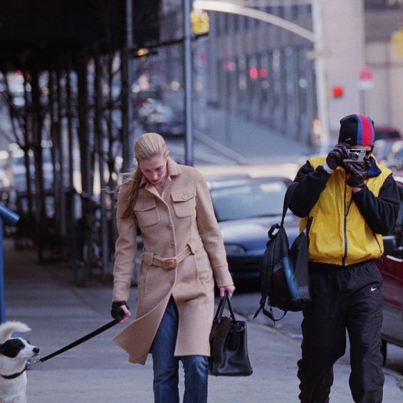 Na vida real, Carolyn Bessette, esposa de John F. Kennedy Jr., foi fotografada em 1998 enquanto passeava com seu cachorro usando o icônico casaco bege da Prada, peça que se tornaria um dos símbolos mais elegantes de seu estilo minimalista dos anos 90