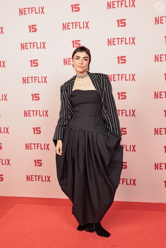 Maria Casadevall: surge com um vestido longo preto de silhueta volumosa e estruturada na saia, combinado com um mini blazer cropped de risca-de-giz por cima dos ombros e gargantilha trançada no pescoço