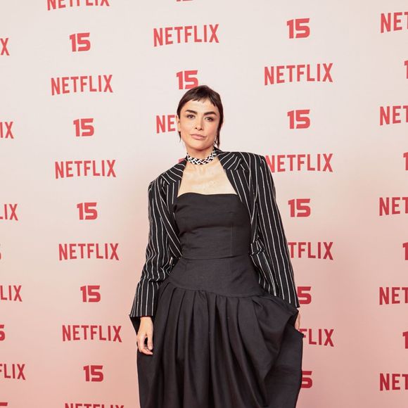 Maria Casadevall: surge com um vestido longo preto de silhueta volumosa e estruturada na saia, combinado com um mini blazer cropped de risca-de-giz por cima dos ombros e gargantilha trançada no pescoço