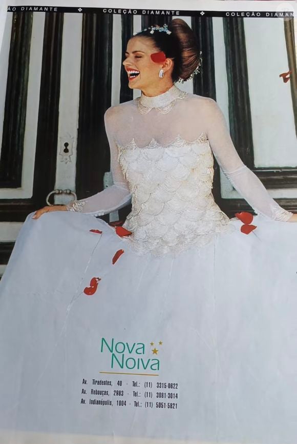 1.Vestido de manga longa em tule

Um clássico das noivas brasileiras do início dos anos 2000. O vestido apresenta uma saia ampla em camadas de tule esvoaçante, com um estilo ousado e romântico. A parte superior tem uma ilusão de transparência com mangas longas em tule, contrastando com bordados em formato de escamas de concha, conferindo brilho e textura. É um look etéreo, quase angelical, mas com um toque dramático pelos detalhes vermelhos.