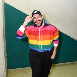 Tiago Abravanel: apresenta um look vibrante e esportivo composto por um moletom de capuz (hoodie) com listras horizontais multicoloridas em padrão arco-íris, combinado com calça de alfaiataria preta de modelagem solta. Ele finaliza a produção com um boné preto da New Balance e tênis de solado tratorado com detalhes coloridos