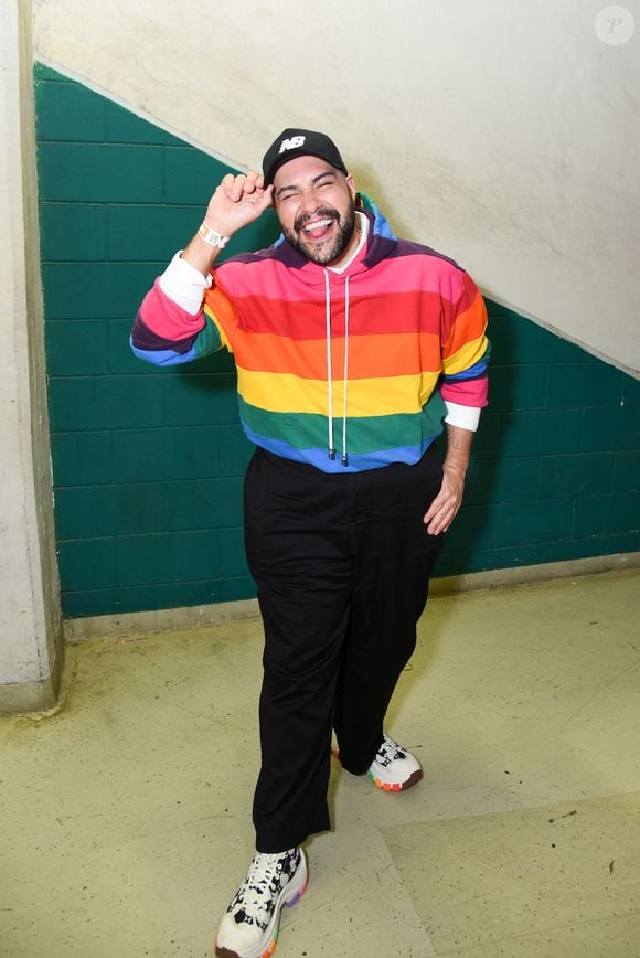 Tiago Abravanel: apresenta um look vibrante e esportivo composto por um moletom de capuz (hoodie) com listras horizontais multicoloridas em padrão arco-íris, combinado com calça de alfaiataria preta de modelagem solta. Ele finaliza a produção com um boné preto da New Balance e tênis de solado tratorado com detalhes coloridos