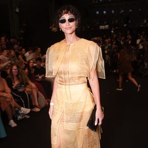 Débora Nascimento personificou o conceito de 'moda-arte' ao surgir com um conjunto de transparências em tom areia. O look é composto por um top cropped e uma saia midi, ambos construídos com sobreposições de retângulos de organza que trazem trechos manuscritos, conferindo uma aura literária e intelectual à produção