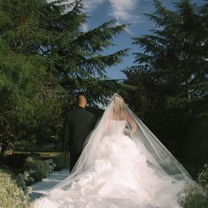 A escolha do vestido seguiu uma estética romântica e atemporal. Com saia volumosa em camadas e estrutura esculpida, o modelo branco transmite sofisticação, enquanto o véu longo adiciona um toque de tradição ao visual.