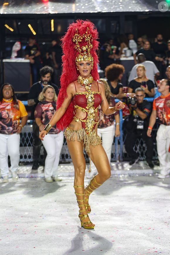 Também musa do Salgueiro, Cintia Dicker elegeu um look mínimo nas cores dourado e vermelho com uma coroa gigantesca