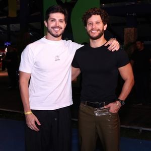 Heron Leal e Igor Cosso: Heron Leal (à esquerda) vestiu uma camiseta branca básica com estampa discreta, calça preta solta e tênis brancos com detalhes cinzas. Igor Cosso (à direita) optou por uma camiseta preta justa, calça de couro marrom-escura brilhante e botas marrons de bico fino, além de um cinto preto de couro e relógio de pulso preto
