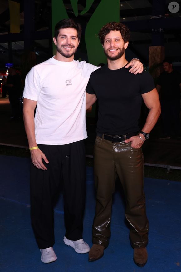 Heron Leal e Igor Cosso: Heron Leal (à esquerda) vestiu uma camiseta branca básica com estampa discreta, calça preta solta e tênis brancos com detalhes cinzas. Igor Cosso (à direita) optou por uma camiseta preta justa, calça de couro marrom-escura brilhante e botas marrons de bico fino, além de um cinto preto de couro e relógio de pulso preto