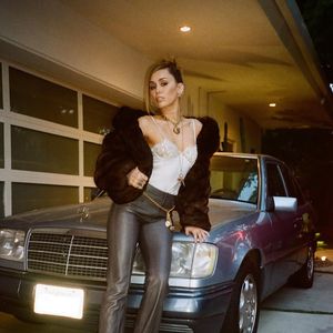 O visual foi complementado por um styling totalmente alinhado à estética Y2K: jaqueta bomber volumosa de pele marrom, calça de couro cinza de modelagem ampla e acessórios marcantes