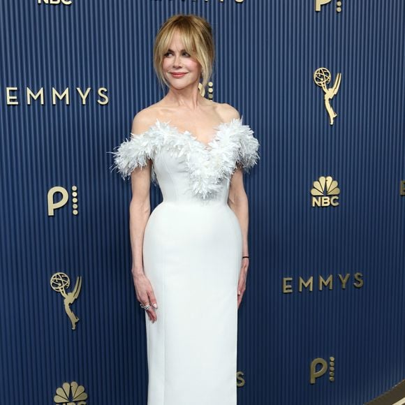 Nicole Kidman optou pela elegância atemporal de um vestido ajustado branco de comprimento midi com caimento estruturado e fenda discreta. O grande destaque da peça é o decote ombro a ombro adornado por plumas delicadas em tom sobre tom que emolduram o colo. Ela finalizou a produção com scarpins pretos clássicos de salto alto, coque despojado com franja solta e maquiagem de acabamento natural