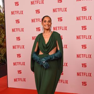 Camila Pitanga: veste um vestido longo verde-escuro drapeado com capa integrada nos ombros e aberturas laterais na cintura, combinado com luvas compridas de tom azul-esverdeado, brincos compridos prateados e sapatos scarpin roxos em contraste
