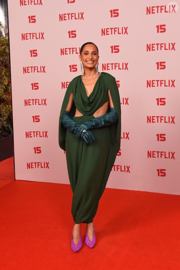Camila Pitanga: veste um vestido longo verde-escuro drapeado com capa integrada nos ombros e aberturas laterais na cintura, combinado com luvas compridas de tom azul-esverdeado, brincos compridos prateados e sapatos scarpin roxos em contraste