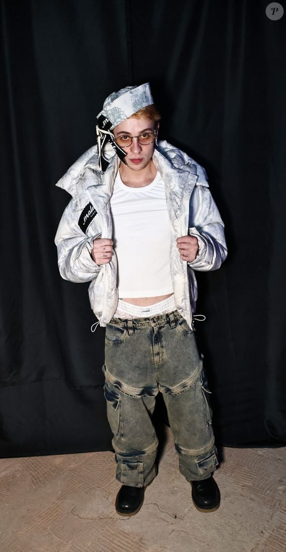 Juliano Floss chamou atenção no evento fashion ao apostar em uma produção urbana com jaqueta puffer clara estampada, camiseta branca e calça jeans cargo oversized. O detalhe mais ousado ficou por conta da cueca branca de renda, com textura vazada e desenho ornamental, deixada à mostra acima da cintura da calça