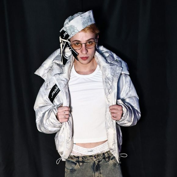 Juliano Floss chamou atenção no evento fashion ao apostar em uma produção urbana com jaqueta puffer clara estampada, camiseta branca e calça jeans cargo oversized. O detalhe mais ousado ficou por conta da cueca branca de renda, com textura vazada e desenho ornamental, deixada à mostra acima da cintura da calça