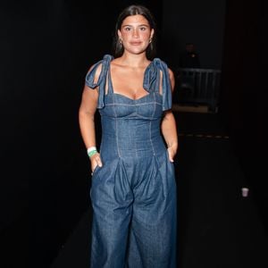 Giullia Buscacio trouxe o jeans para o patamar da alta costura com um macacão utilitário de lavagem escura e modelagem imponente. A peça conta com um bustiê estruturado de decote coração e alças largas finalizadas em laços volumosos nos ombros, fundindo o peso do denim com detalhes românticos