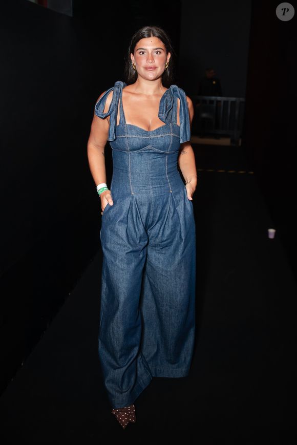 Giullia Buscacio trouxe o jeans para o patamar da alta costura com um macacão utilitário de lavagem escura e modelagem imponente. A peça conta com um bustiê estruturado de decote coração e alças largas finalizadas em laços volumosos nos ombros, fundindo o peso do denim com detalhes românticos
