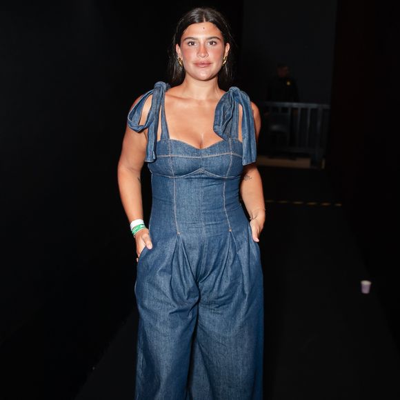 Giullia Buscacio trouxe o jeans para o patamar da alta costura com um macacão utilitário de lavagem escura e modelagem imponente. A peça conta com um bustiê estruturado de decote coração e alças largas finalizadas em laços volumosos nos ombros, fundindo o peso do denim com detalhes românticos