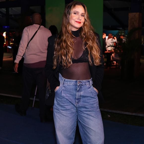 Aline Fanju combinou casualidade e sofisticação em um look moderno. Ela vestiu uma blusa preta de tule transparente com gola alta, revelando um sutiã de renda por baixo, sobreposta por um blazer preto clássico. A produção se completou com calça jeans baggy de lavagem clara e sapatos mocassim tratorados em couro preto com fivela dourada