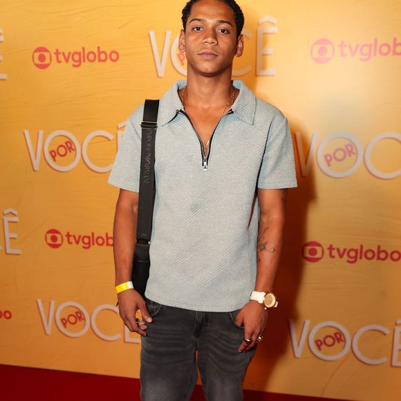 Apresenta um visual streetwear com camisa polo azul-claro texturizada e fecho em zíper, acompanhada de jeans cinza-escuro com lavagem estonada. Acessórios como bolsa tiracolo, relógio de pulseira branca e tênis pretos fecham a composição