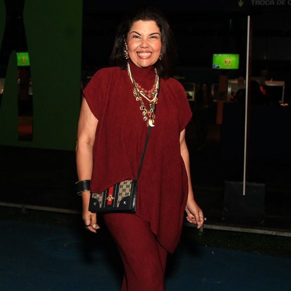Fabiana Karla elege um conjunto monocromático texturizado em tom de vermelho-vinho (burgundy), formado por uma blusa de gola alta e caimento assimétrico sem mangas sobreposta a uma calça de corte flare no mesmo tecido. Como acessórios de destaque, usa um maximalista mix de colares de pedrarias e pérolas, além de uma bolsa transversal Gucci com estampa de monograma clássico