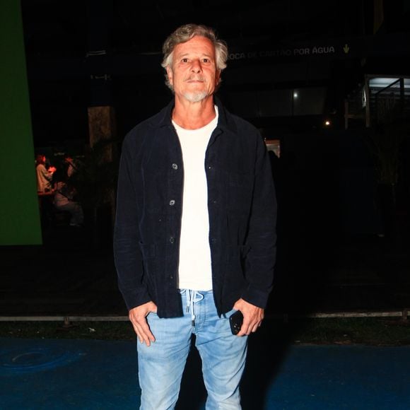 Marcello Novaes comparece ao evento com um visual casual e confortável, composto por uma jaqueta de veludo cotelê azul-marinho usada aberta sobre uma camiseta básica branca lisa. Para finalizar a produção descontraída, o ator veste uma calça jeans clara de lavagem estonada com amarração no cós e tênis casuais de camurça bege
