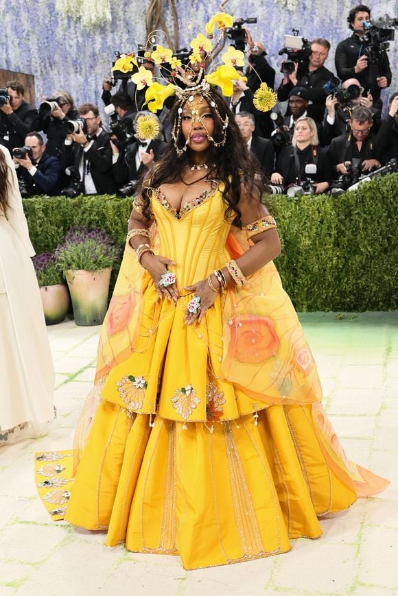 A cantora SZA no Met Gala 2026 entregou maximalismo em um vestido amarelo repleto de bordados, com aplicações e um acessório de cabeça que trouxe um ar místico ao look