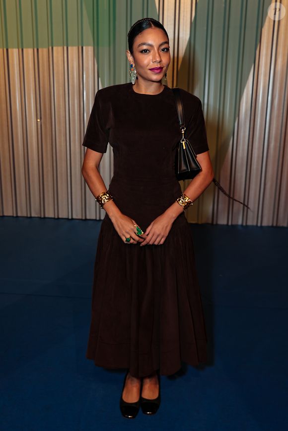 A cantora Any Gabrielly optou por uma elegância clássica e imponente, vestindo um conjunto de camurça em tom marrom chocolate, cor que foi protagonista absoluta desta edição. O visual consiste em um top de mangas curtas e gola careca, combinado a uma saia midi plissada de cintura marcada, criando uma silhueta atemporal