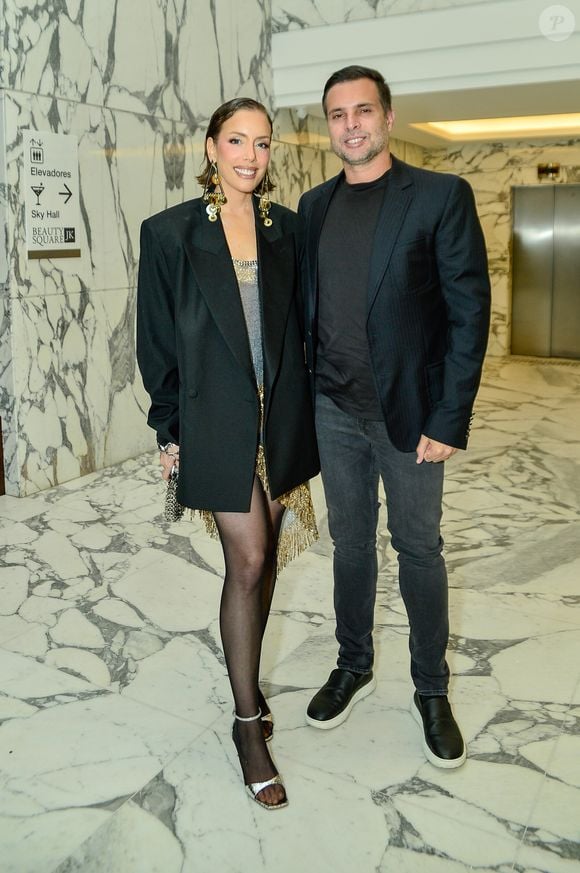 Fabiana Justus equilibrou o corte masculino de um blazer oversized preto de alfaiataria com a sensualidade de um vestido curto metalizado com detalhes em dourado e barra assimétrica de franjas. A influenciadora digital arrematou a composição com meia-calça fina preta, sandálias de tiras finas prateadas e maxibrincos geométricos em tom de ouro velho que emolduraram seu penteado de efeito molhado