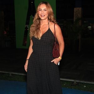 Paolla Oliveira surge elegante em um macacão pantacourt xadrez em tons escuros de marrom e preto, caracterizado por decote em V transpassado e alças finas. A atriz arremata a produção sofisticada com botas de bico fino pretas, uma bolsa tiracolo texturizada em tom de vinho e colares dourados delicados