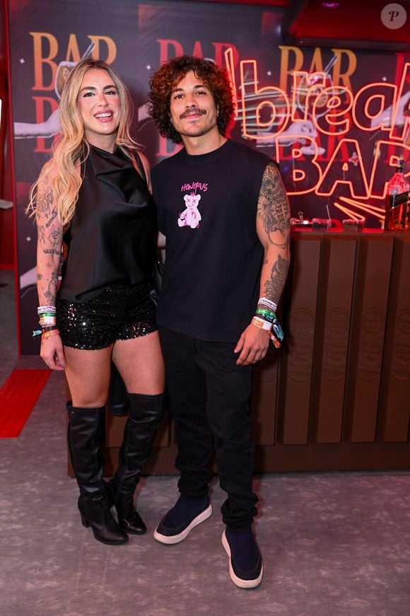 Douglas Sampaio e Camila Gentile: o ator aposta em uma regata machão preta com estampa gráfica de ursinho, calça jeans preta reta e tênis escuro de sola branca. Já sua companheira usa um top de cetim preto com gola degagê, shorts de paetês pretos, botas de cano alto over the knee e acabamento acetinado
